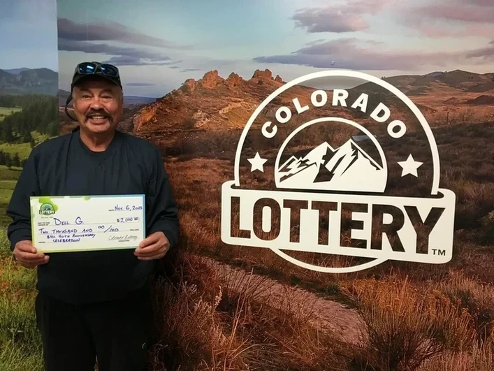戴尔·G.在科罗拉多彩票背景前举著$2,000的支票